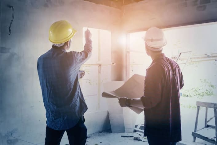 Engenheiro e profissional da construção civil verificando uma obra.